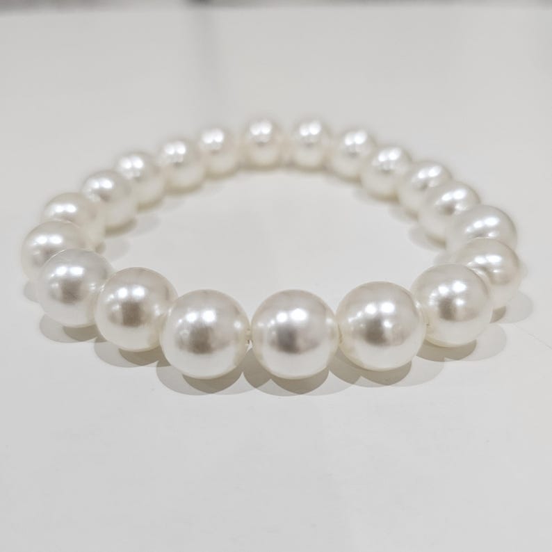May include: A white pearl bracelet with large, round beads. The beads are strung together on an elastic band, creating a simple yet elegant accessory. The bracelet is shown on a white surface.