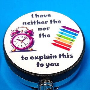 May include: Two retractable badge holders with a white background and black text. The text on the badge holder reads "I have neither the time nor the energy to explain this to you". The badge holder also features a cartoon alarm clock and crayons.