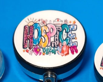 May include: Three colorful retractable badge reels with a white background and the word "HOSPICE" in a colorful, stylized font. The reels have a black plastic base and a silver metal clip.