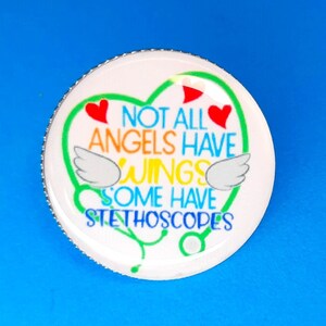 May include: White heart-shaped button with a silver rim. The button has a green stethoscope design with red hearts and the text "Not all angels have wings some have stethoscopes".