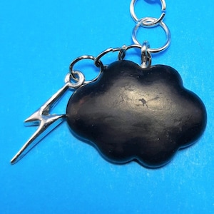 May include: A black cloud charm with a silver lightning bolt charm attached to a silver chain with a lobster clasp.