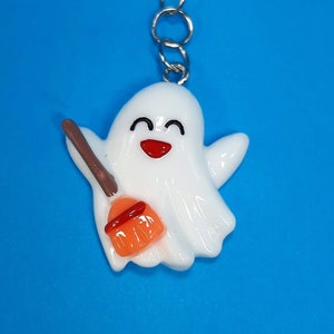 May include: A white ghost with a happy face holding a brown and orange broom. The ghost is attached to a silver chain.