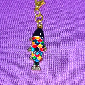 May include: A gold charm with a black and colorful fish design. The fish has a black body with colorful scales and a gold fin.