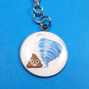 May include: A silver charm with a white background featuring a brown poop emoji being blown away by a blue tornado.