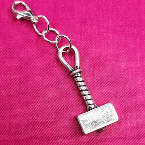 May include: A silver charm in the shape of a hammer with a twisted handle and a silver chain attached.