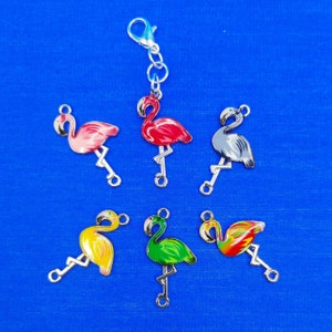 May include: A set of ten colorful flamingo charms, each with a silver loop for attaching to a keychain, bracelet, or other jewelry. The charms are painted in various colors, including pink, red, green, yellow, and gray.