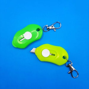 May include: Two green keychain utility knives with a silver key ring. One knife has a white button and the other has a white button and a silver blade.