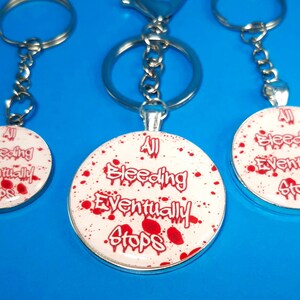 May include: Three silver keychains with round white and red enamel charms. The charms have the text "All Bleeding Eventually Stops" in red and white lettering with red splatter paint.
