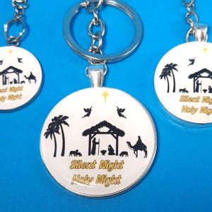 May include: Three silver keychains with round glass charms featuring a black silhouette of the nativity scene with palm trees and the text "Silent Night Holy Night" in gold lettering.