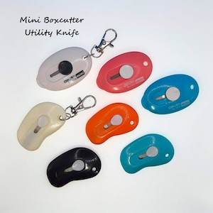 May include: Six colorful mini box cutters with keychains. The box cutters are shaped like a teardrop and have a silver blade. The text "OLFA mini" is printed on each box cutter.