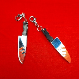 May include: Two silver keychains shaped like knives with red and orange paint splatter designs.