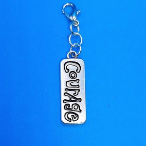 May include: Silver charm with a silver chain and a rectangular tag that says "Courage" in a stylized font.