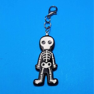 May include: A black and white skeleton keychain with a silver chain. The skeleton is standing with its arms at its sides and has a skull for a head.