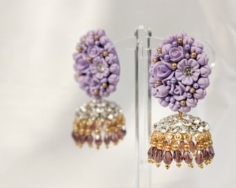 Può includere: Un paio di orecchini floreali color lavanda con dettagli dorati e perline di cristallo e viola pendenti.