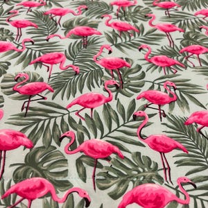 Op de afbeelding: Een stof met een herhalend patroon van roze flamingo's en groene tropische bladeren op een lichtblauwe achtergrond. De flamingo's zijn in verschillende poses afgebeeld en de bladeren zijn gedetailleerd. Het ontwerp is helder en tropisch.