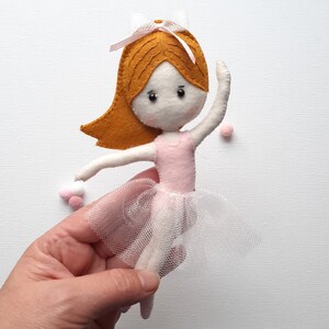 May include: A felt ballerina doll with a pink dress and a white tulle skirt. The doll has brown hair and black eyes.