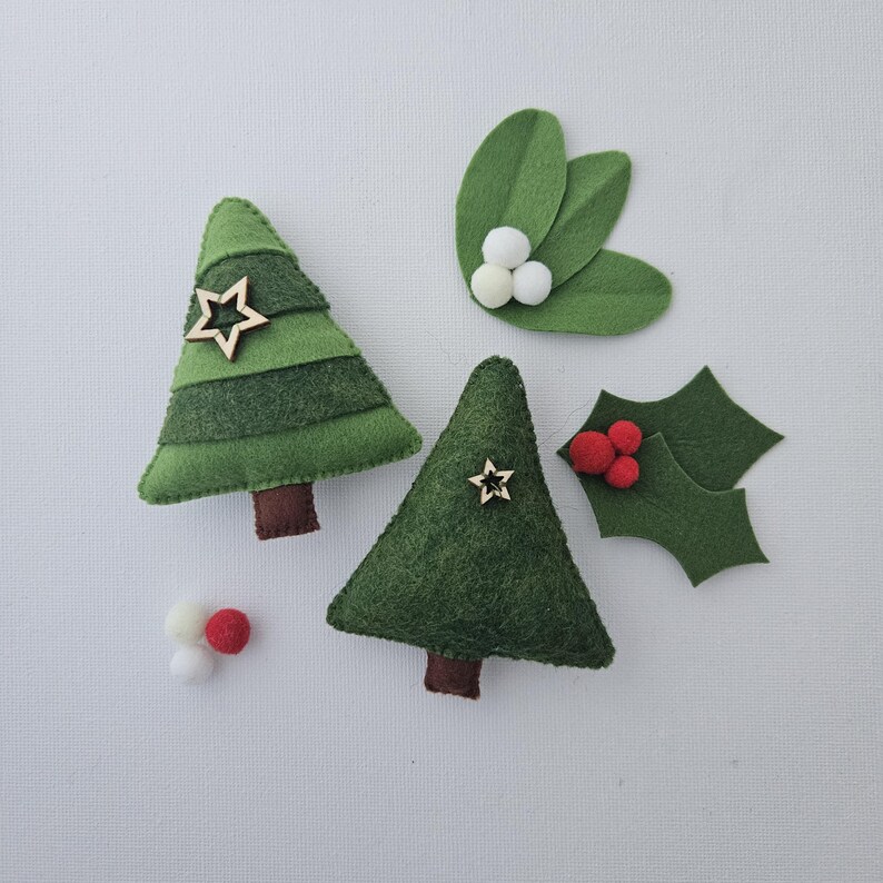May include: A collection of handmade felt Christmas ornaments. The set includes two green Christmas trees with wooden star accents, holly leaves with red berries, and mistletoe with white pom-poms.