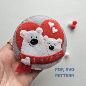 May include: Felt appliqué pattern for two polar bears in a red heart with a red scarf. The pattern is available in PDF and SVG formats.