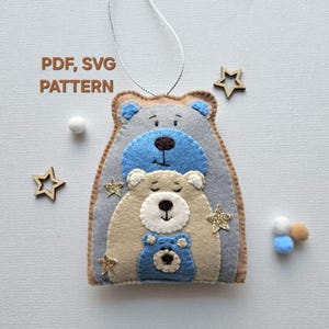 May include: A felt ornament featuring three stacked bears. The largest bear is gray, the middle bear is beige, and the smallest bear is blue. Each bear has a white face with black eyes and a black nose. The bears are decorated with gold glitter stars.