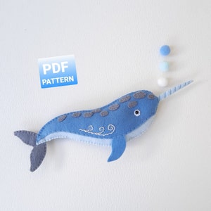 May include: A blue felt narwhal with a white horn and a black eye. The narwhal is embroidered with white swirls. The image includes the text "PDF PATTERN".