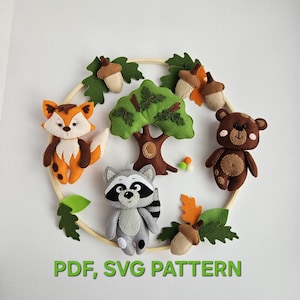 Puede incluir: Móvil de fieltro con temática de bosque que presenta un zorro, un mapache y un oso, junto con un árbol, bellotas y hojas. El diseño está dispuesto en forma circular. El texto "PDF, SVG PATTERN" es visible en la parte inferior.