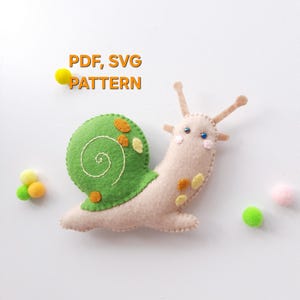 May include: A felt snail craft with a beige body and a green shell featuring orange and yellow spots. The text PDF, SVG PATTERN is displayed above the snail. Small colourful pom-poms are scattered around the snail on a plain white background.