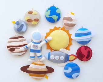May include: Felt astronaut, sun, and planets in blue, red, yellow, brown, and gray colors. The planets have rings and the sun has rays. The astronaut is wearing a white spacesuit with a blue belt and a red helmet.