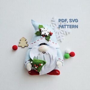 May include: A light blue felt gnome with a white beard and a pointed hat, holding a green felt Christmas tree. The gnome is decorated with a snowflake, red berries, and a wooden tree. Text on the image reads "PDF, SVG PATTERN".
