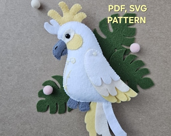 May include: A felt cockatoo with white, yellow, and gray details, surrounded by green felt leaves and small pink pom-poms. The text "PDF, SVG PATTERN" is visible. This craft project is ideal for creating felt animal decorations.