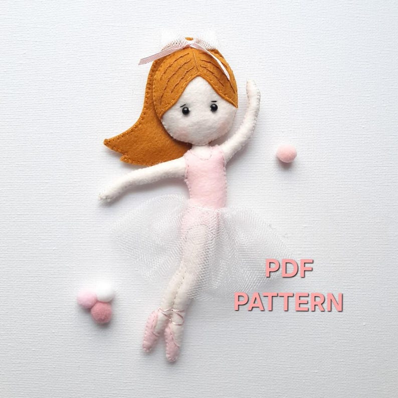 May include: A felt ballerina doll with brown hair, a pink leotard, and a white tulle skirt. The doll is holding a pink pom-pom in her hand. The text "PDF PATTERN" is written in pink letters on a white background.
