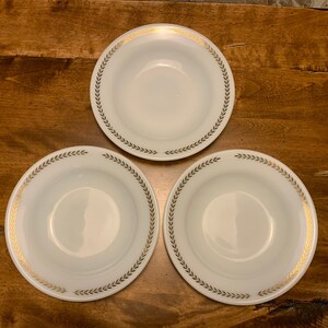 May include: Three white ceramic bowls with gold leaf trim. The bowls have a simple design with a repeating pattern of leaves around the rim.