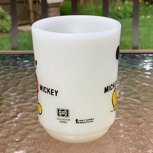 May include: White ceramic mug with a black and red Mickey Mouse illustration on one side and a black and yellow Mickey Mouse illustration on the other side. The mug has the text "Mickey" on both sides. The mug also has a black and white Pepsi Collector Series logo and a black and white Walt Disney Productions logo.