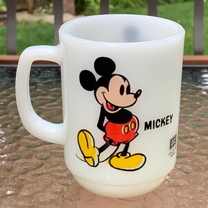 May include: White ceramic mug with a cartoon image of Mickey Mouse in red shorts and yellow shoes. The mug has the word "MICKEY" printed on the side.