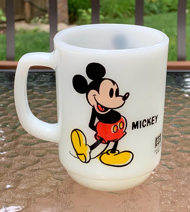 May include: White ceramic mug with a cartoon image of Mickey Mouse in red shorts and yellow shoes. The mug has the word "MICKEY" printed on the side.
