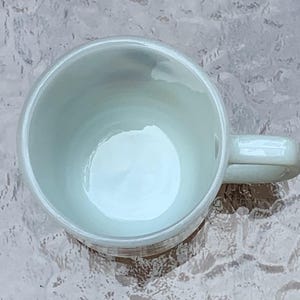 May include: A white ceramic coffee mug with a handle. The mug is empty and has a smooth, glossy finish.