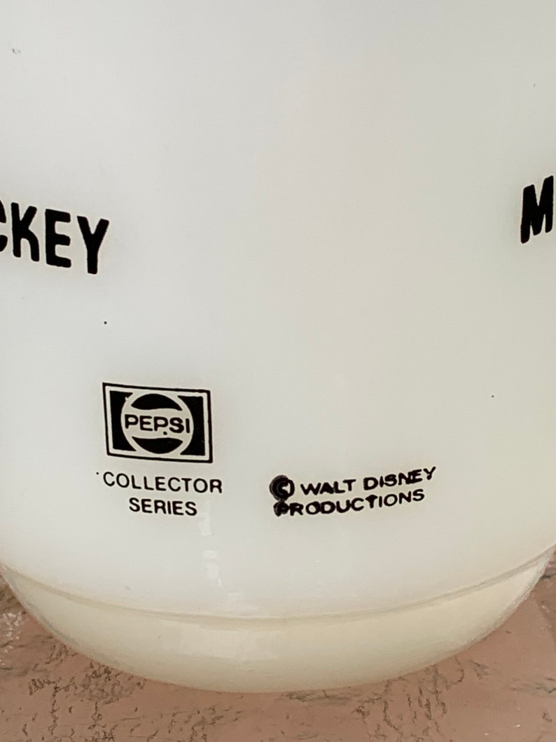 May include: White ceramic Mickey Mouse mug with black lettering and a Pepsi logo. The mug is part of a collector series and features the Walt Disney Productions logo.