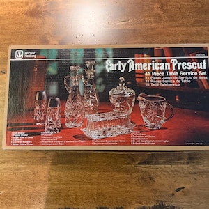 May include: A box for an 11-piece Early American Prescut table service set. The box features a photo of the crystal pieces, including a sugar bowl, creamer, and decanter. The text on the box reads "Early American Prescut 11 Piece Table Service Set".