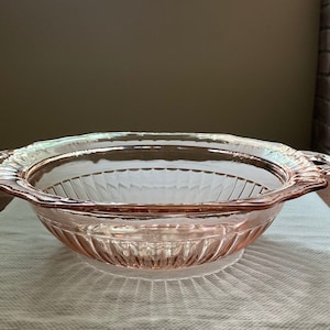 May include: A vintage pink glass bowl with two handles. The bowl has a fluted design and is perfect for serving salads, fruit, or other dishes.