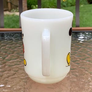 May include: White ceramic mug with a cartoon image of Mickey Mouse in red, yellow, and black. The mug has a handle.
