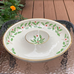 May include: A white ceramic serving dish with a gold rim and a holly design. The dish has a smaller bowl in the center for dipping.