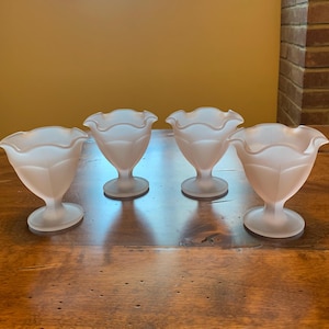 May include: Four frosted glass dessert dishes with a scalloped rim. The dishes are white and have a delicate, feminine design.