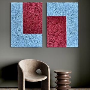Könnte beinhalten: Zwei abstrakte Wandkunstwerke. Jedes hat eine strukturierte Oberfläche mit hellblauem Hintergrund und einer rechteckigen kastanienbraunen Form. Die Kunst wird über einem beigen Stuhl mit kreisförmigem Ausschnitt und einem braunen Beistelltisch ausgestellt.