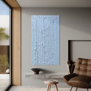May include: A rectangular, light blue abstract painting with vertical textured lines. The artwork is displayed on a gray wall in a modern living space, complemented by a brown leather armchair and a wooden side table.