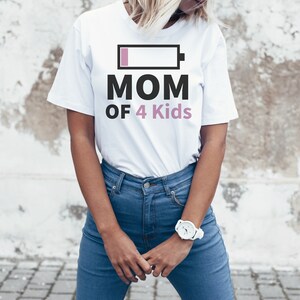 Può includere: Maglietta bianca con una grafica nera e rosa di un'icona di batteria scarica e il testo "MOM OF 4 Kids".