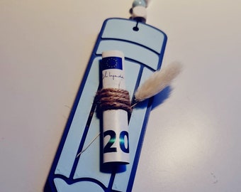 Könnte beinhalten: Ein blauer Bleistift-Anhänger mit einem darin eingerollten Zwanzig-Euro-Schein, der mit Schnur gebunden ist. Der Anhänger hängt an einer weißen und blauen Perlenkette.
