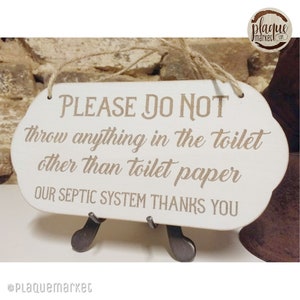 Pode incluir: Uma placa de madeira branca com borda decorativa e barbante de juta para pendurar. A placa diz: "PLEASE DO NOT throw anything in the toilet other than toilet paper OUR SEPTIC SYSTEM THANKS YOU."