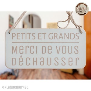 Peut inclure: Une pancarte en bois bleu clair avec le texte "Petits et Grands Merci de vous déchausser" en lettres blanches. La pancarte est suspendue à une ficelle.