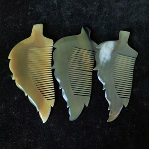 May include: Three leaf-shaped combs in varying shades of tan and green. Each comb features a handle that resembles a leaf, with fine teeth for combing hair. The combs are made of a natural material, possibly horn or bone.
