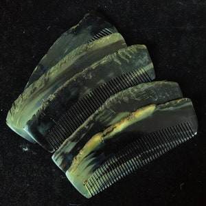 May include: A collection of four handcrafted combs. Each comb features a dark, marbled pattern with shades of black, gray, and hints of yellow and green. The combs have a natural, textured edge and fine teeth for grooming.
