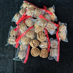 May include: A collection of brown, textured walnut shells individually packaged in small, clear plastic bags with red zip-lock seals. The shells are arranged in a loose pile, showcasing their intricate, ridged, and organic exterior surfaces.